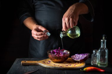 Aşçı taze kırmızı lahana salatasına zeytinyağı döker. Lokanta mutfağında sağlıklı yemekler pişirmek..