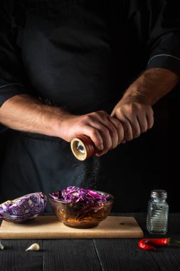 Aşçı taze kırmızı lahana salatasına biber ekler. Lokanta mutfağında sağlıklı yemekler pişirmek..