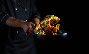 Şef kızartma tavasında sebze hazırlar. Sağlıklı vejetaryen yemekleri ve yemekleri karanlık bir arka planda pişirmek. Ücretsiz reklam alanı.