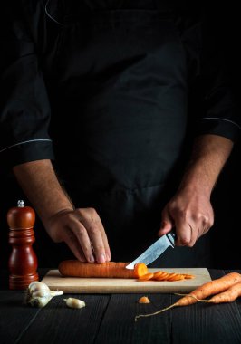 Aşçı restoran mutfağında sebze çorbası için havuç kesiyor. İş sırasında şefin ellerini yakın plan çek. Havuç diyeti