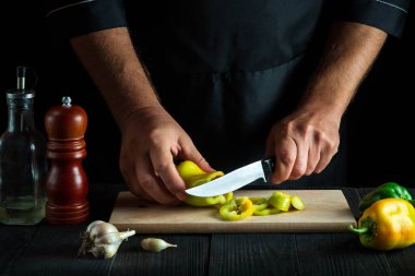 Şef restoran mutfağında salata için dolmalık biber kesiyor. Çalışırken bir aşçının ellerini yakın plan çek