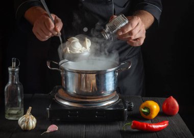 Şef restoranın mutfağında bir tencerede hamur tatlısı hazırlıyor. Aşçının yakın çekim elleri tuz ekler..