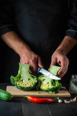 Aşçı taze Brokoli 'yi bıçak ile keser. Salata için mutfak masasında taze sebzelerle birlikte. Yemek ve restoran veya kafe konsepti.