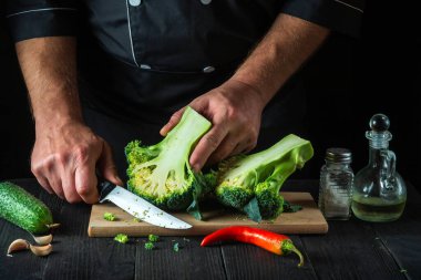 Şef taze Brokoli 'yi bıçak ile kesiyor. Salata için mutfak masasında taze sebzelerle birlikte. Yemek ve restoran veya kafe konsepti.