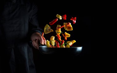 Şef kızartma tavasında sebze hazırlar. Siyah arka planda sağlıklı vejetaryen yemeği ve yemek pişirmek. Ücretsiz reklam alanı