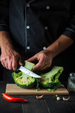 Profesyonel şef taze Brokoli 'yi bıçak ile kesiyor. Antika mutfak masasında salata için taze sebzelerle birlikte. Yemek ve restoran veya kafe konsepti