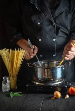 Şef sebzeli bir tencerede İtalyan makarnası hazırlıyor. Lokanta mutfağında yemek pişirirken ellerin yakın plan çekimi.