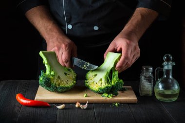 Şef taze Brokoli 'yi bıçak ile kesiyor. Salata için mutfak masasında taze sebzelerle birlikte. Yemek ve restoran veya kafe konsepti.