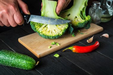 Profesyonel şef taze Brokoli 'yi bıçak ile kesiyor. Antika mutfak masasında salata için taze sebzelerle birlikte. Yemek ve restoran veya kafe konsepti