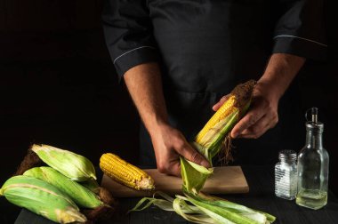 Profesyonel şef pişirmeden önce olgun mısırı kabuğundan soyar. Restoranın mutfağında çalışma ortamı. Çalışırken aşçının elleri yakın plan çekimde. Ücretsiz reklam alanı