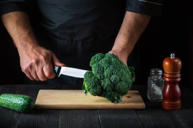 Aşçı taze Brokoli 'yi bıçak ile keser. Salata için mutfak masasında taze sebzelerle birlikte. Yemek ve restoran veya kafe konsepti.