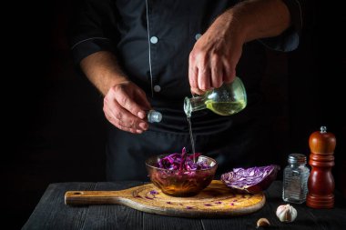 Profesyonel bir şef taze kırmızı lahana salatasına zeytinyağı döker. Lokanta mutfağında sağlıklı yemekler pişirmek.