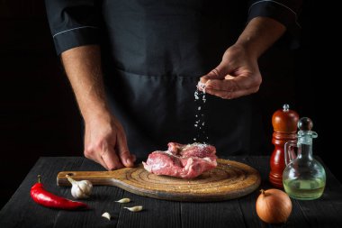 Aşçı ete tuz serper. Pişirmeden önce et hazırlıyorum. Restoranın mutfağında çalışma ortamı.