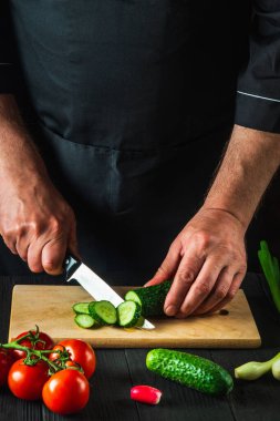 Aşçı ya da aşçı salata için bir restoranın mutfağında yeşil salatalık keser. Sebze diyeti ya da abur cubur fikri.