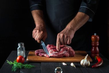 Şef mutfakta bir bıçakla et keser ve yemek hazırlar. Bir restoranda lezzetli bir öğle yemeği hazırlamak için mutfak masasındaki sebze ve baharatlar..