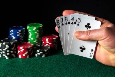 Floş kombinasyonlu poker kartları. Kumarbazın eli kumarhanede iskambil kağıdı tutar. Çipler yeşil masada.