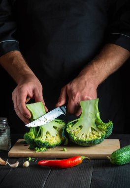 Şef taze Brokoli 'yi bıçak ile kesiyor. Salata için mutfak masasında taze sebzelerle birlikte. Yemek ve restoran veya kafe konsepti
