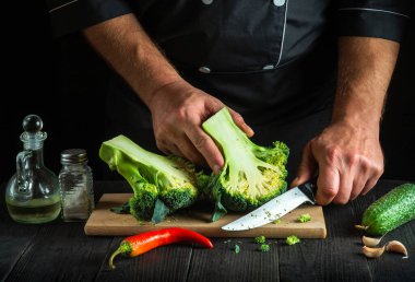 Profesyonel şef taze Brokoli 'yi bıçak ile kesiyor. Antika mutfak masasında salata için taze sebzelerle birlikte. Yemek ve restoran veya kafe konsepti