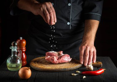 Aşçı ete tuz serper. Pişirmeden önce et hazırlıyorum. Restoranın mutfağında çalışma ortamı.