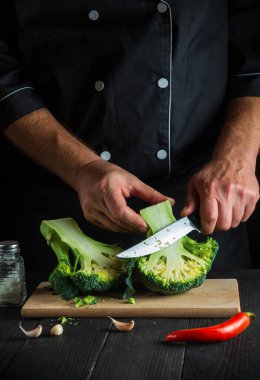 Aşçı taze Brokoli 'yi bıçak ile kesiyor. Antika mutfak masasında salata için taze sebzelerle birlikte. Yemek ve restoran veya kafe konsepti
