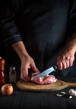 Aşçı mutfakta bir bıçakla et keser ve yemek hazırlar. Lezzetli bir öğle yemeği hazırlamak için restoranda bir masada sebze ve baharat..