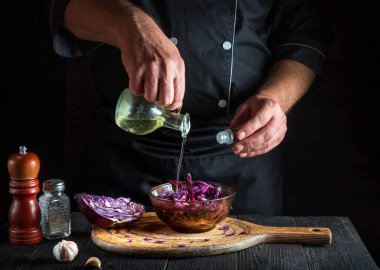 Profesyonel aşçı taze kırmızı lahana salatasına zeytinyağı döker. Lokanta mutfağında sağlıklı yemekler pişirmek..