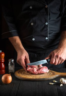 Aşçı mutfakta bir bıçakla et keser ve yemek hazırlar. Lezzetli bir öğle yemeği hazırlamak için restoranda bir masada sebze ve baharat.