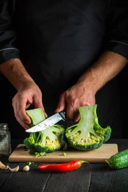 Şef taze Brokoli 'yi bıçakla doğruyor. Antika mutfak masasında salata için taze sebzelerle birlikte. Yemek ve restoran veya kafe konsepti.