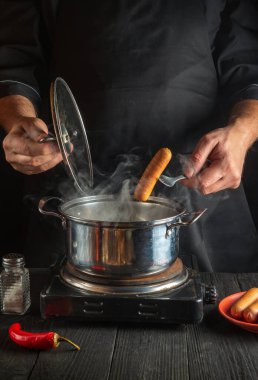 Şef bir tencereye Viyana sosisi koyar. Bir restoranın ya da kafenin mutfağında çalışma ortamı. Kahvaltı veya öğle yemeği hazırlıyorum..