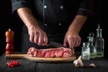 Şef pişirmeden önce eti bıçakla keser. Lezzetli bir öğle yemeği hazırlamak için restoranın mutfak masasındaki baharatlar.