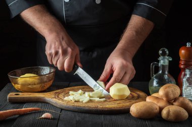 Şef kahvaltı ya da akşam yemeği hazırlamadan önce çiğ patatesleri bıçakla parçalara ayırır. Lokanta mutfağında çalışırken aşçıya yakın çekim.
