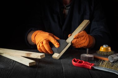 Bir marangoz ahşap bir kalası aşındırıcı bir aletle cilalar. İş sırasında inşaatçının elleri yakın plan. Yenileme veya inşaat fikri.