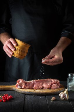 Şef çiğ et hazırlıyor. Aşçı pişirmeden önce bifteğe tuz ekler. Ulusal yemek restoranın mutfağında hazırlanıyor..