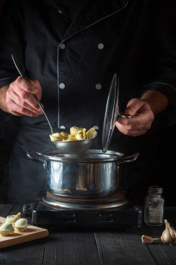 Profesyonel şef, restoranın mutfağında bir tencerede pelmeni hazırlıyor. Çalışırken bir aşçının ellerini yakın plan çek