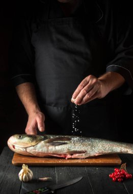 Şef restoranın mutfağında gümüş sazan balığı hazırlıyor. Aşçı balığın üzerine tuz serper. Mutfak masasında çalışma ortamı