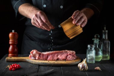 Professional chef prepares raw veal meat. Before baking, the chef adds salt to the beef. National dish is being prepared in the restaurant kitchen.