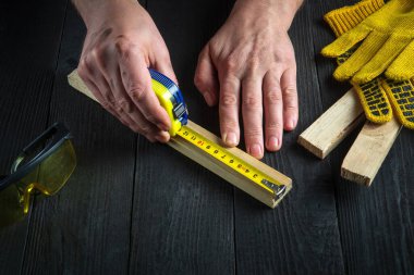 Marangoz ya da marangoz bir tahta parçasının uzunluğunu ölçmek için bir inşaat bandı kullanır. İşyerindeki ustanın elleri. Marangozluk atölyesinde çalışma ortamı.