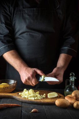 Şef kahvaltı ya da akşam yemeği hazırlamadan önce çiğ patatesleri bıçakla parçalara ayırır. Lokanta mutfağında çalışırken aşçıya yakın çekim.