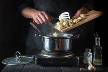 Şef restoranın mutfağında bir tencerede pelmeni hazırlıyor. Çalışırken bir aşçının ellerini yakın plan çek.