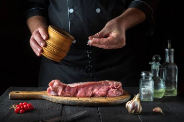 Şef çiğ dana eti hazırlar. Aşçı pişirmeden önce bifteğe tuz ekler. Ulusal yemek restoranın mutfağında hazırlanıyor..