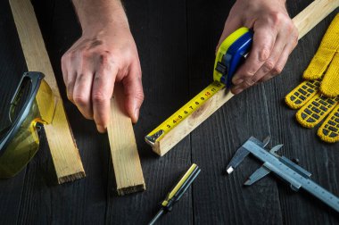 Profesyonel marangoz ya da marangoz bir tahta parçasının uzunluğunu ölçmek için bir inşaat bandı kullanır. İşyerindeki ustanın elleri. Marangozluk atölyesinde çalışma ortamı