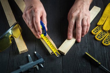 Profesyonel marangoz ya da marangoz bir tahta parçasının uzunluğunu ölçmek için bir inşaat bandı kullanır. İşyerindeki ustanın elleri. Marangozluk atölyesinde çalışma ortamı