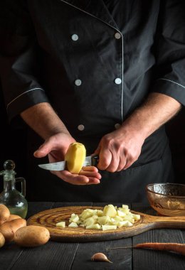 Şef kahvaltıyı ya da akşam yemeğini hazırlamadan önce çiğ patatesleri bıçakla parçalara ayırır. Lokanta mutfağında çalışırken aşçı ellerinin yakın çekimi.