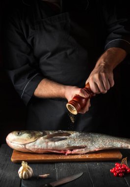 Şef restoranın mutfağında sazan balığı hazırlıyor. Aşçı balığın üzerine biber serper. Mutfak masasında çalışma ortamı