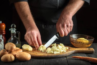 Şef çiğ patatesleri küçük parçalara ayırmak için bir bıçak kullanır. Lokanta mutfağında çalışırken aşçıya yakın çekim.