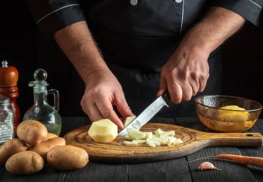 Aşçı kahvaltı ya da akşam yemeği hazırlamadan önce çiğ patatesleri bıçakla parçalara ayırır. Lokanta mutfağında çalışırken aşçı ellerinin yakın çekimi.