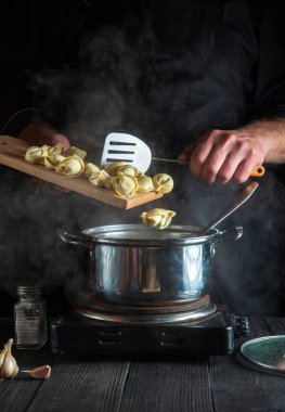 Aşçı restoranın mutfağında bir tencerede pelmeni hazırlıyor. Çalışırken aşçı ellerinin yakın çekimi.