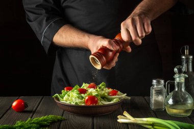 Şef restoranın mutfağında taze sebze salatasına biber ekliyor. Bir değirmeni tutan aşçı ellerinin yakın çekimi. Sağlıklı ve lezzetli yemekler pişirmek..