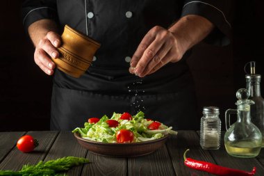 Profesyonel şef ahşap masada taze sebze salatasına tuz serpiyor. Mutfakta sağlıklı yemek hazırlıyorum..