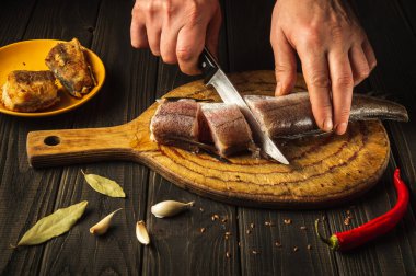 Aşçının eli bıçakla taze Merluccius balığını tahta bir kesme tahtasıyla kesti. Eşsiz bir tarifle ulusal bir balık yemeğinin ev yemeği.